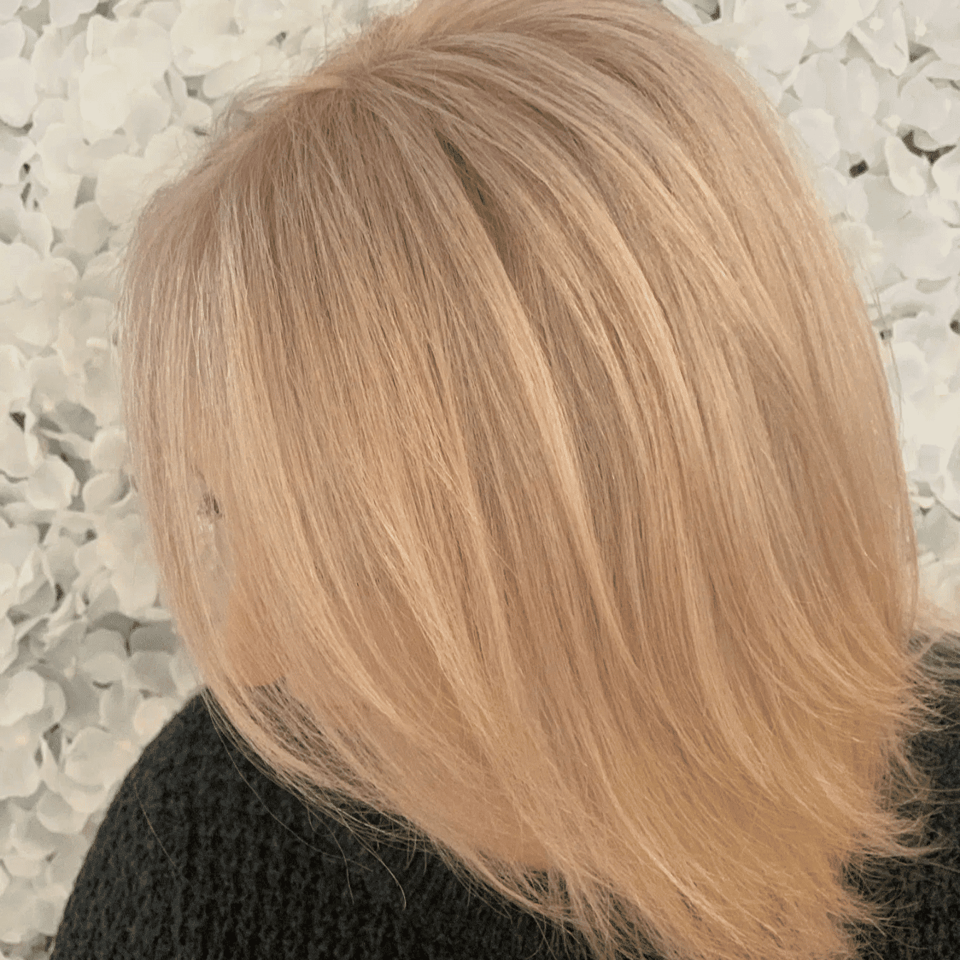 Woman with blonde hair against a floral white background, wearing a black textured sweater.