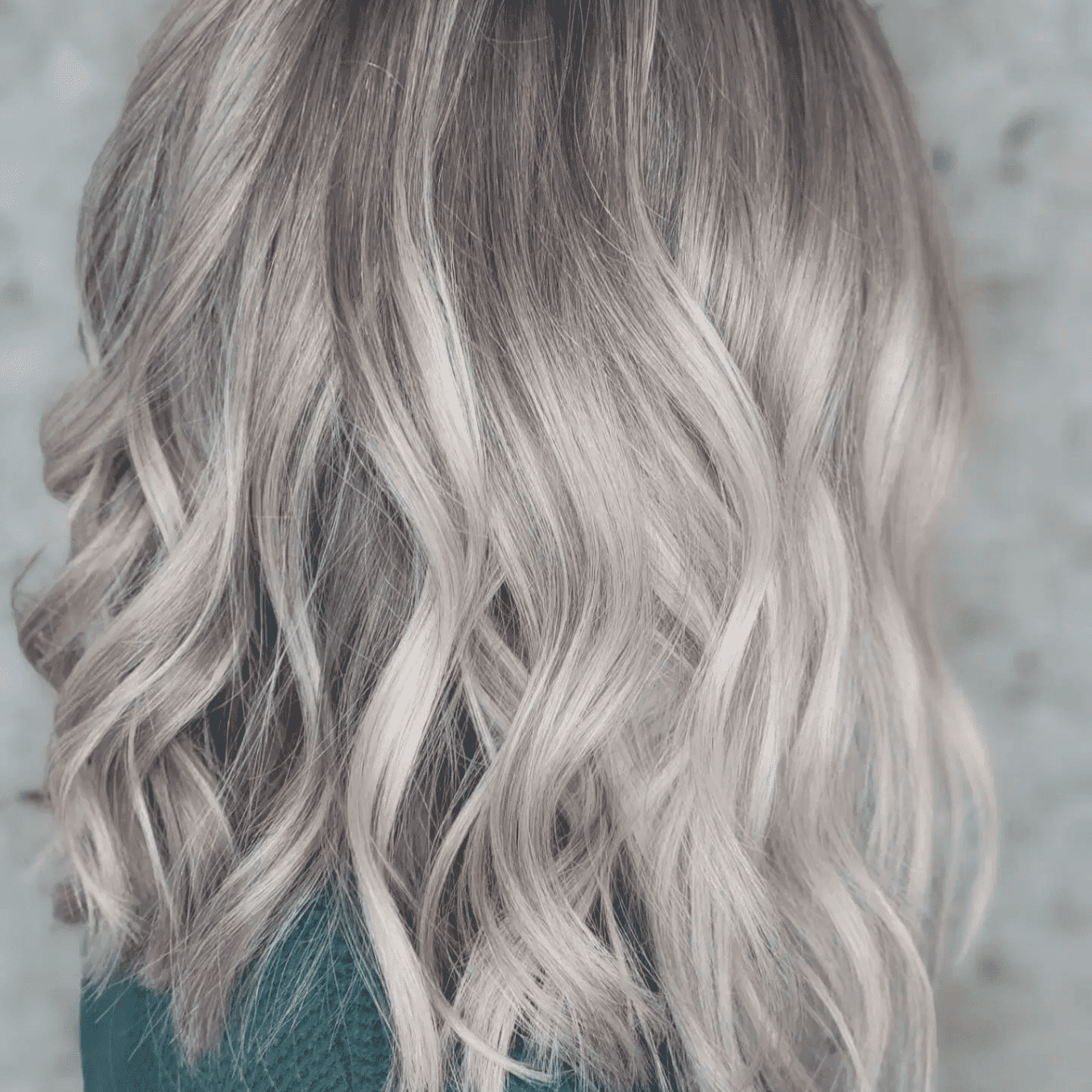 Wavy, shoulder-length, blonde-highlighted hairstyle on a person with dark roots wearing green.